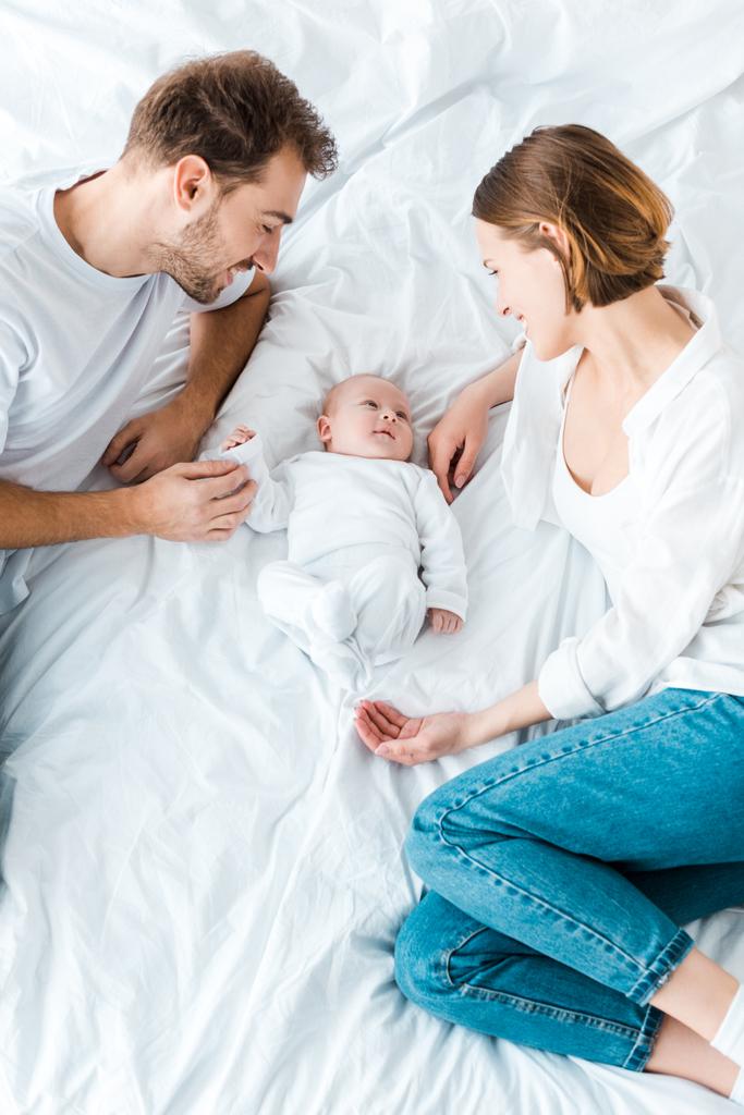 Padres felices tumbados en sábanas blancas y mirando al bebé
 - Foto, Imagen