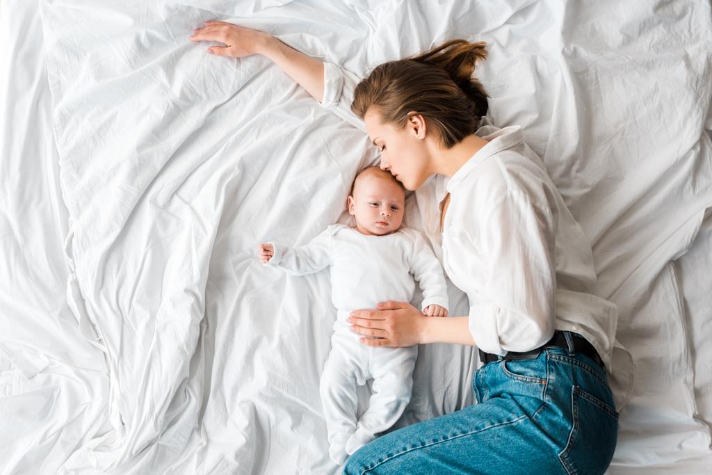 赤ちゃんとベッドに横たわっているジーンズの母親のトップビュー - 写真・画像