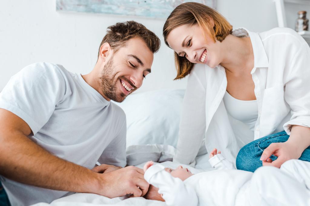 Jovens pais felizes olhando para o bebê na cama
 - Foto, Imagem