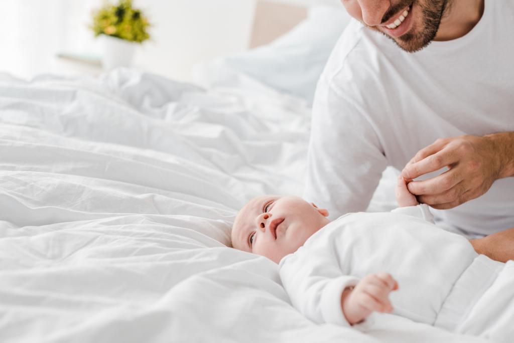 Ausgeschnittener Blick auf glücklichen jungen Vater, der mit Baby im Bett liegt - Foto, Bild