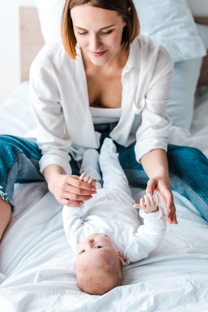 joven madre en camisa blanca jugando con el bebé en la cama
 - Foto, imagen