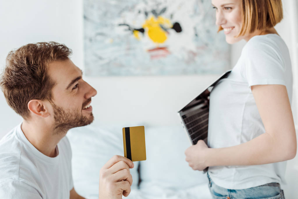 χαμογελαστός ζευγάρι με φορητό υπολογιστή και πιστωτική κάρτα κοιτάζοντας ο ένας τον άλλο - Φωτογραφία, εικόνα