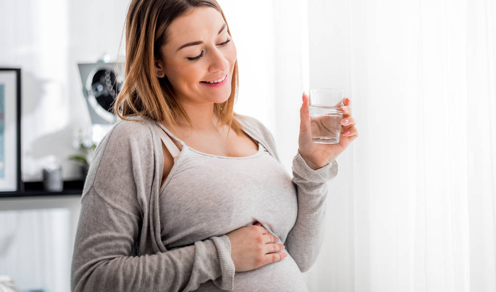 Здоровье во время беременности, беременная женщина пьет воду сидя на диване
 - Фото, изображение