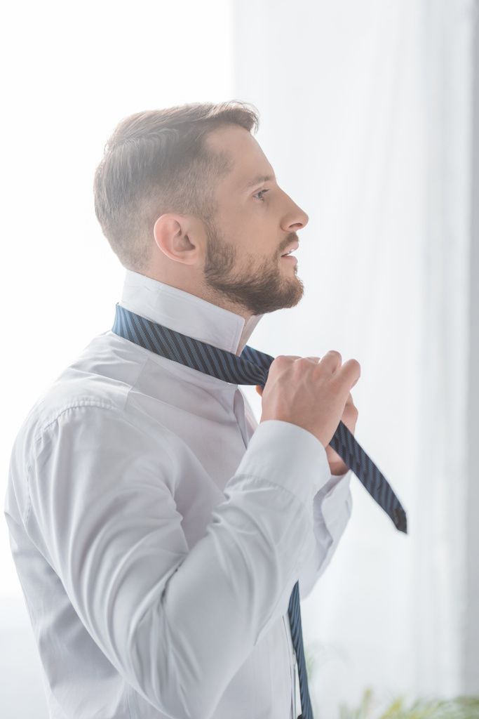knappe bebaarde man in wit shirt aanraken stropdas  - Foto, afbeelding