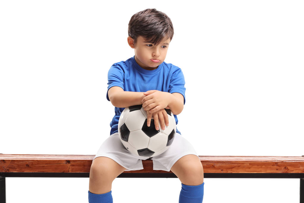 Szomorú kisfiú a futball ül egy fa padon izolált fehér háttér - Fotó, kép