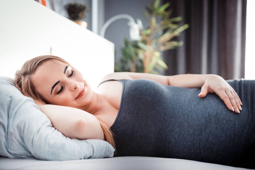 Fiatal terhes nő ül az ágyban, és megérintette a hasát, gyermek elvárás koncepció - Fotó, kép
