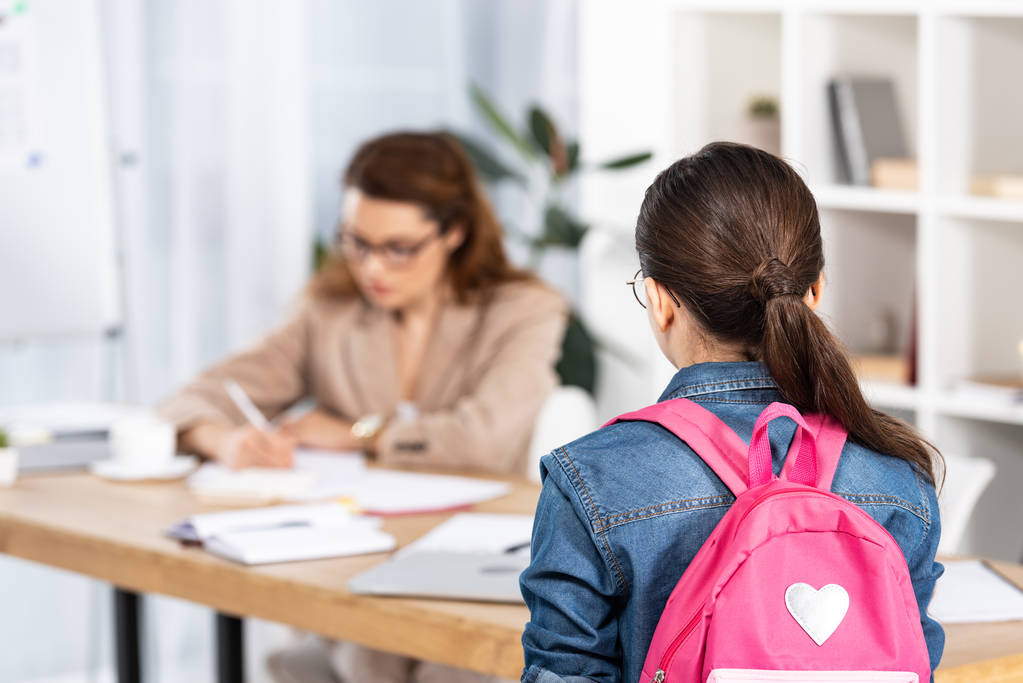 Rückansicht eines Kindes mit pinkfarbenem Rucksack, das neben der Mutter im Büro steht  - Foto, Bild
