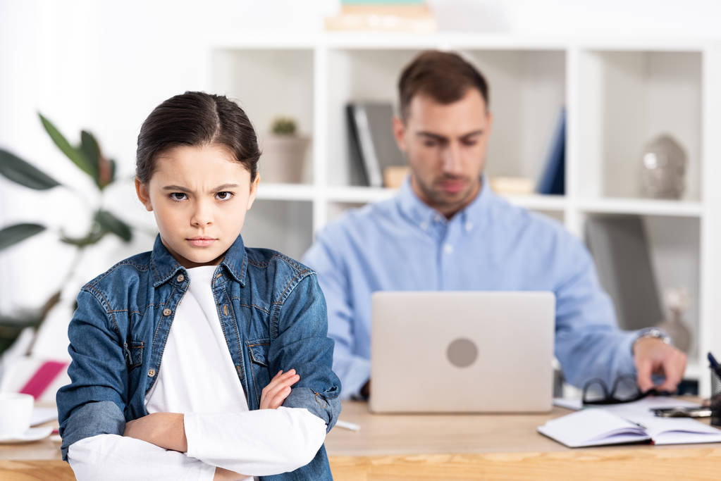 selective focus of upset kid standing with crossed arms near father in office  - Photo, Image