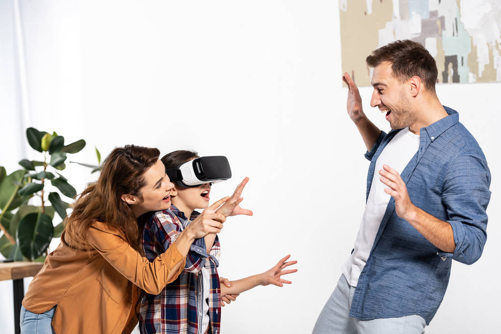 happy mother and cheerful kid in virtual reality headset gesturing near man  - Photo, Image