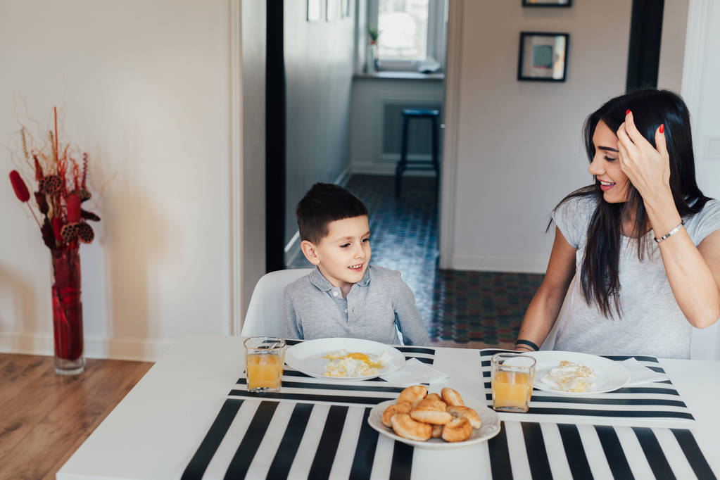 Hermosa mujer joven en casa con su pequeño hijo lindo están desayunando
. - Foto, imagen