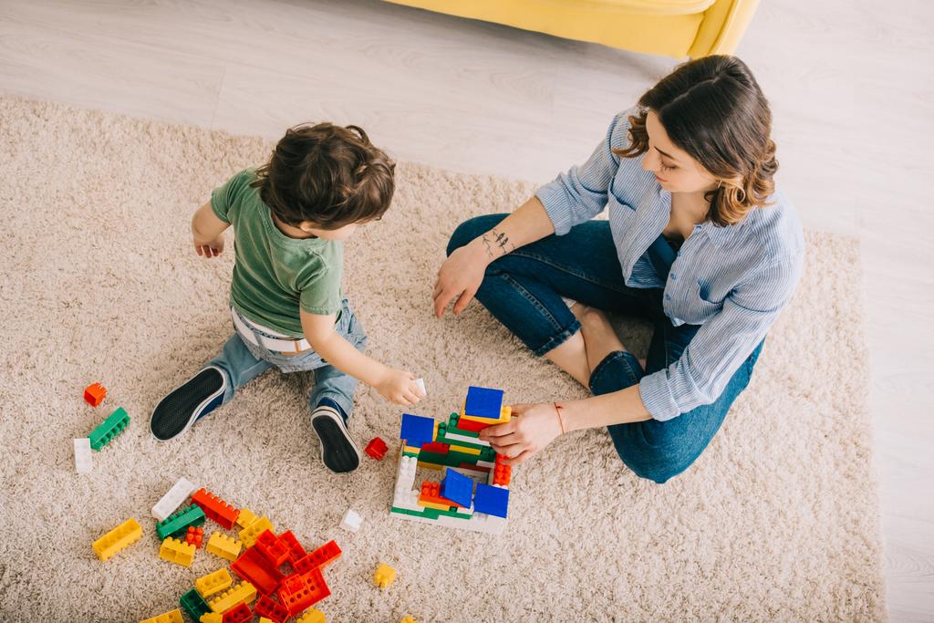 Vista de ángulo alto de mamá e hijo jugando con bloques de juguete en la sala de estar
 - Foto, Imagen