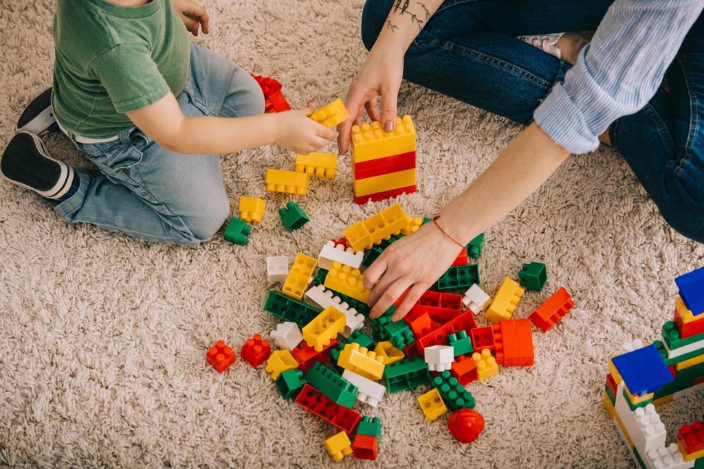 カーペットの上におもちゃのブロックで遊ぶママと息子のトリミングビュー - 写真・画像