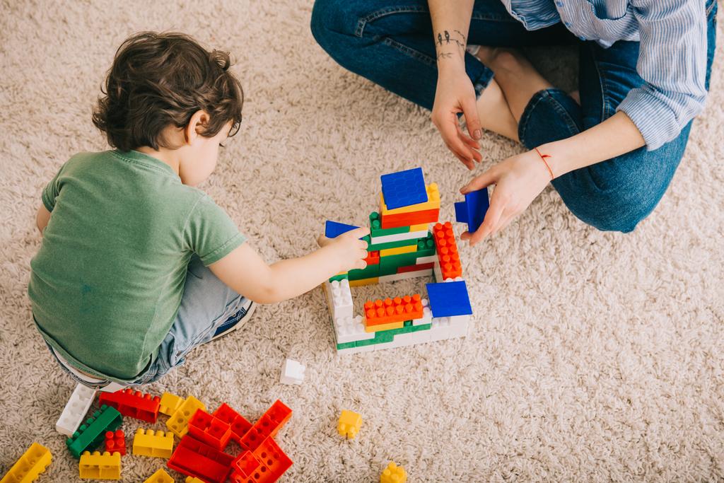Vista ritagliata di mamma e figlio che giocano con blocchi di giocattoli su tappeto
 - Foto, immagini