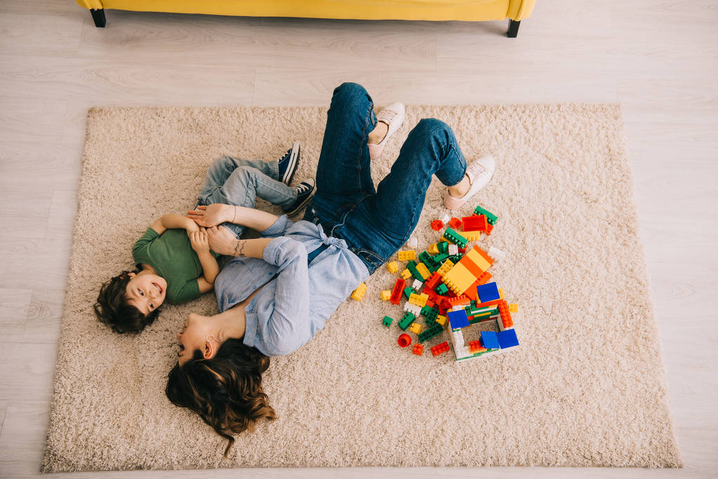 おもちゃのブロックでカーペットの上に横たわっている笑顔のお母さんと息子のオーバーヘッドビュー - 写真・画像