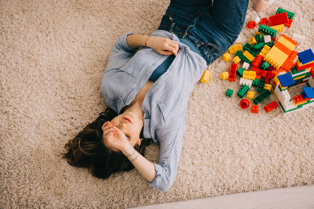 Trübe Sicht auf müde Frau, die mit bunten Spielzeugklötzen auf Teppich liegt - Foto, Bild
