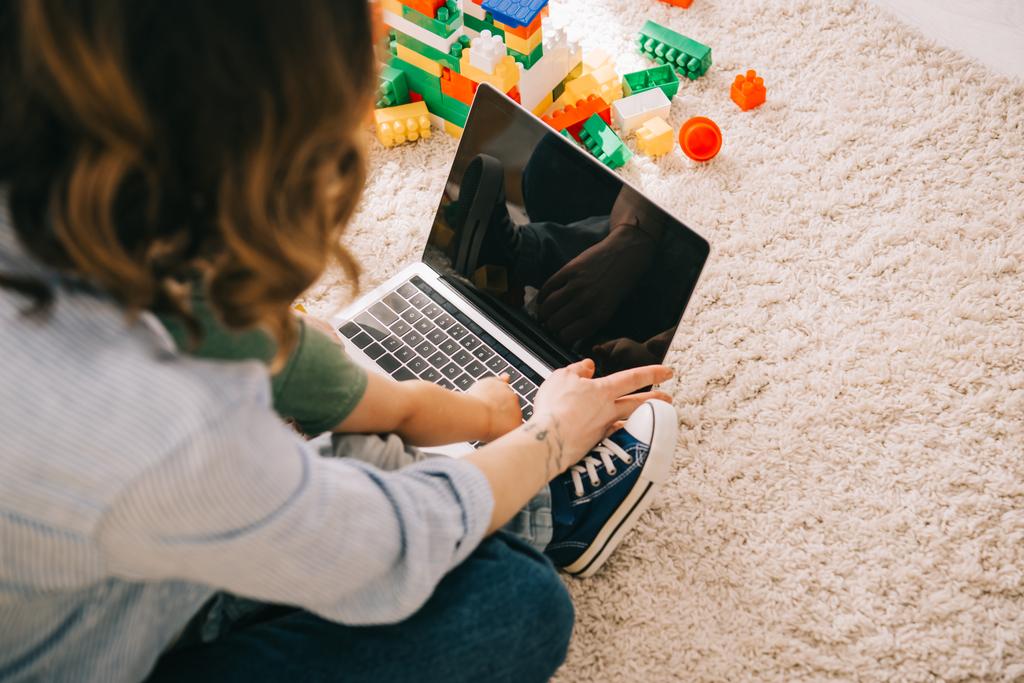 Обрізаний вид на матір і сина, що сидить на килимі і використовує ноутбук
 - Фото, зображення