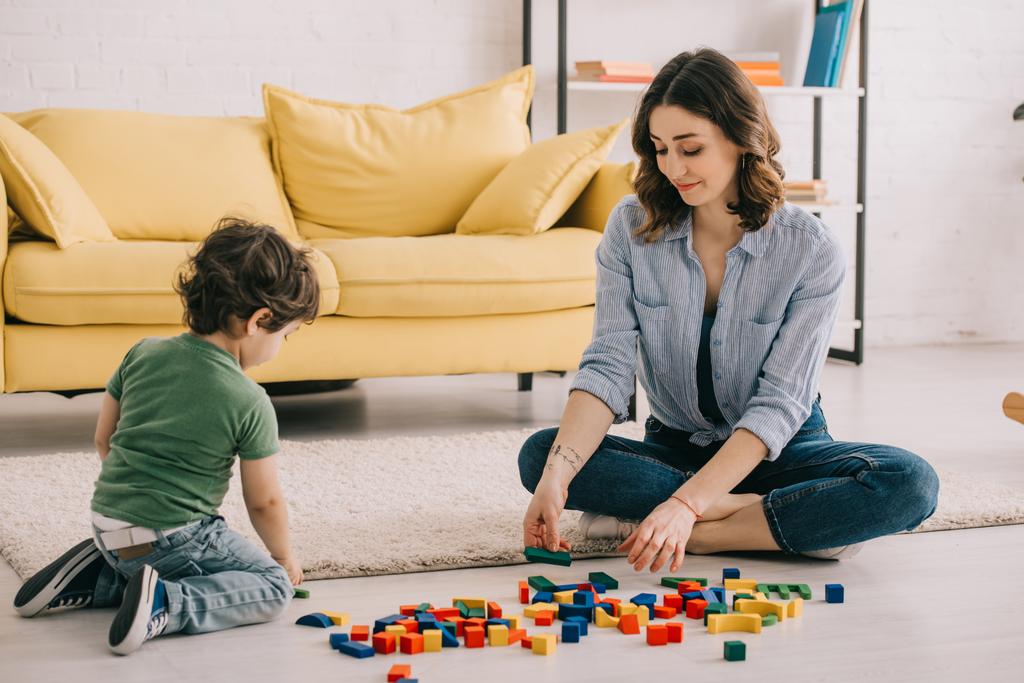 Мать и сын играют с игрушечными блоками на ковре
 - Фото, изображение