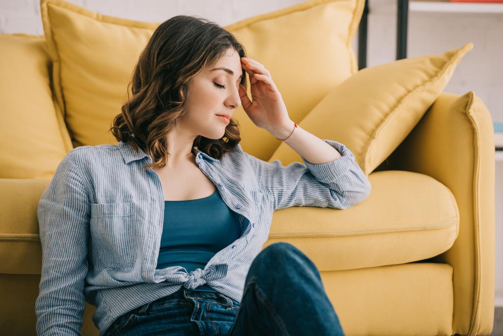 Müde Frau sitzt mit geschlossenen Augen neben gelbem Sofa - Foto, Bild
