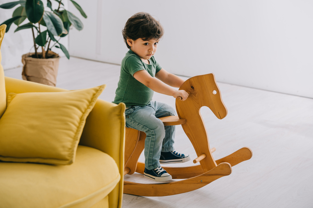 Roztomilá chlapeček sedící na dřevěném houpacím koni v obýváku - Fotografie, Obrázek