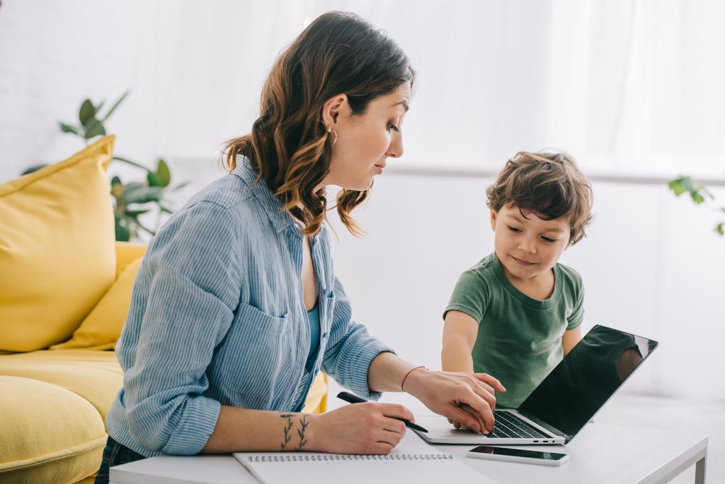 παιδί αγγίζοντας το πληκτρολόγιο φορητού υπολογιστή, ενώ η μητέρα εργάζεται στο σπίτι - Φωτογραφία, εικόνα