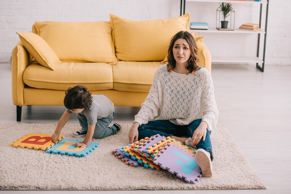 verdrietig moeder en zoon spelen met alfabet puzzel mat op tapijt - Foto, afbeelding