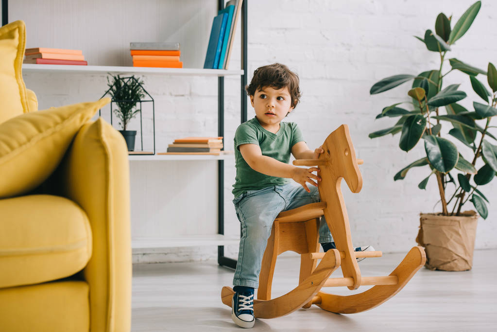 Cute dziecko siedzi na drewnianym konia na biegunach w salonie - Zdjęcie, obraz
