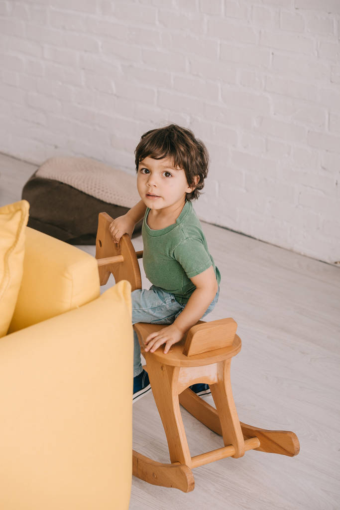 kid sitting on wooden rocking horse in living room - Photo, Image