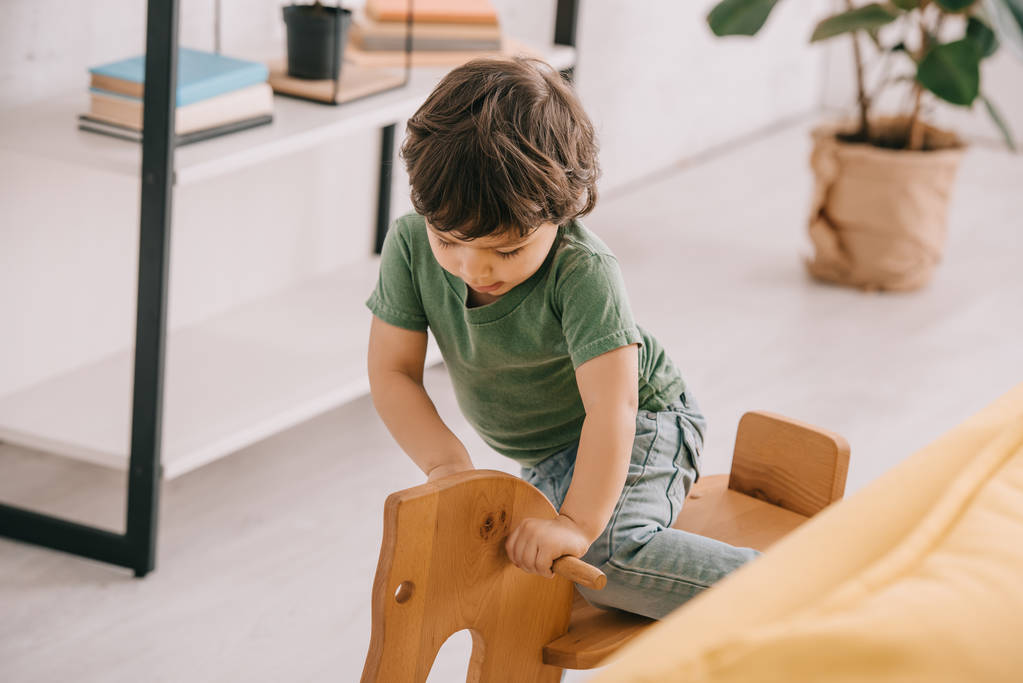 kid in green t-shirt playing with wooden rocking horse - Photo, Image