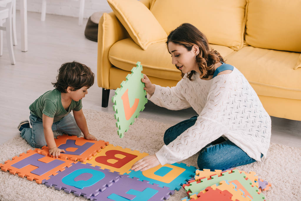 Mother and son playing with alphabet puzzle mat on carpet - Photo, Image