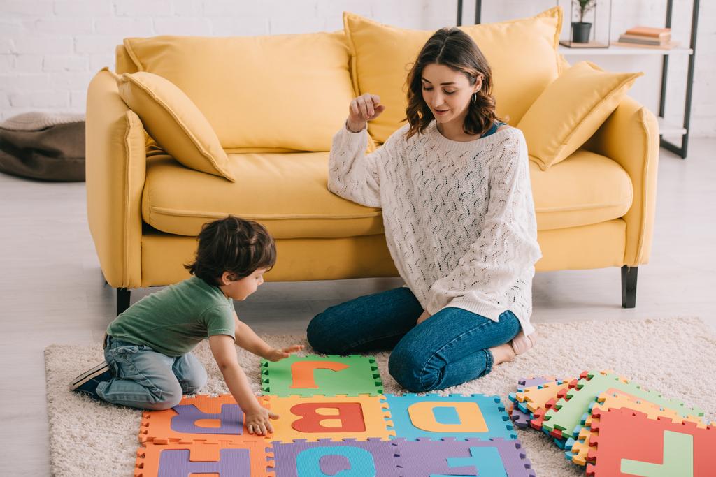 Мать и сын играют в алфавитный коврик-головоломку на ковре
 - Фото, изображение