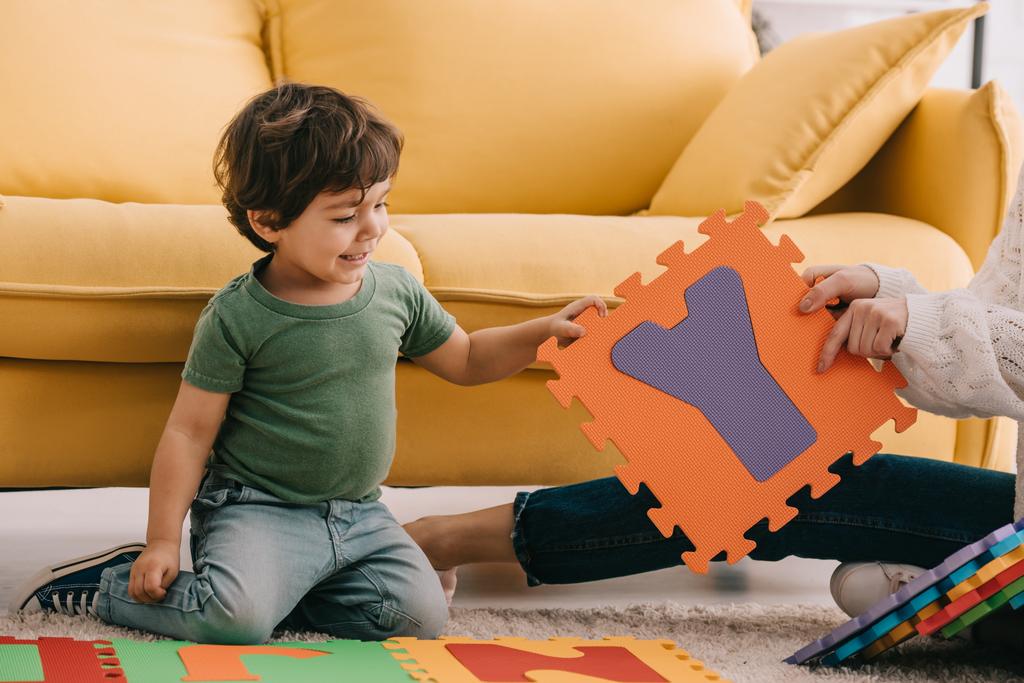 bijgesneden beeld van moeder en zoon spelen met alfabet puzzel mat op tapijt - Foto, afbeelding