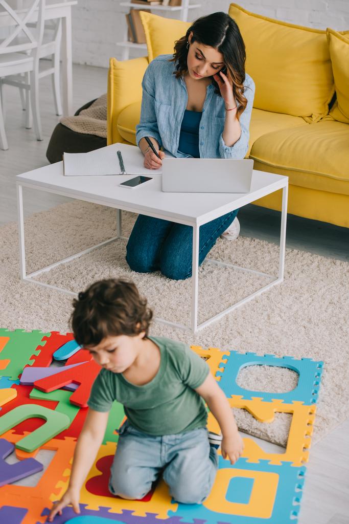 bambino giocando con puzzle mat mentre la madre di lavoro wih laptop
 - Foto, immagini