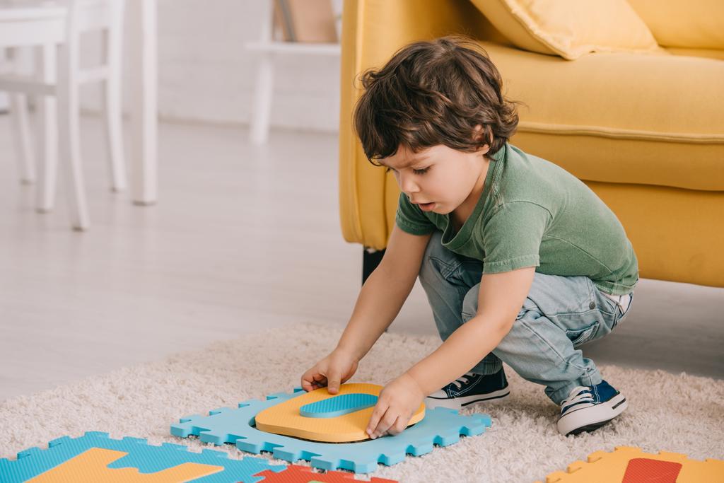 garoto concentrado em t-shirt verde jogando com tapete de quebra-cabeça
 - Foto, Imagem