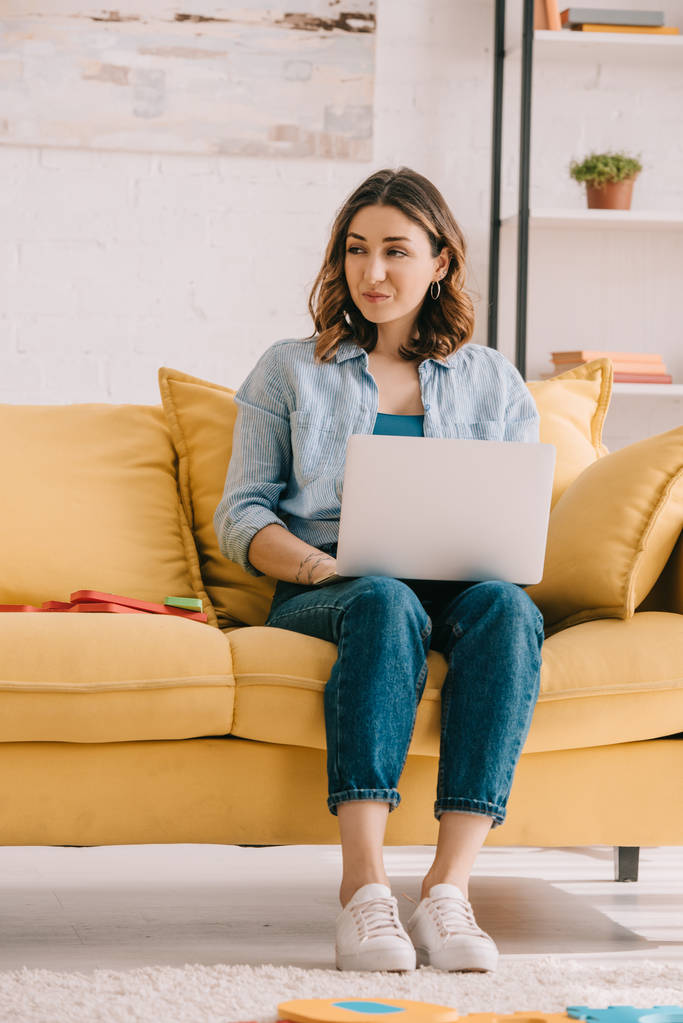 Atractivo freelancer sentado en un sofá amarillo y usando un portátil
 - Foto, Imagen