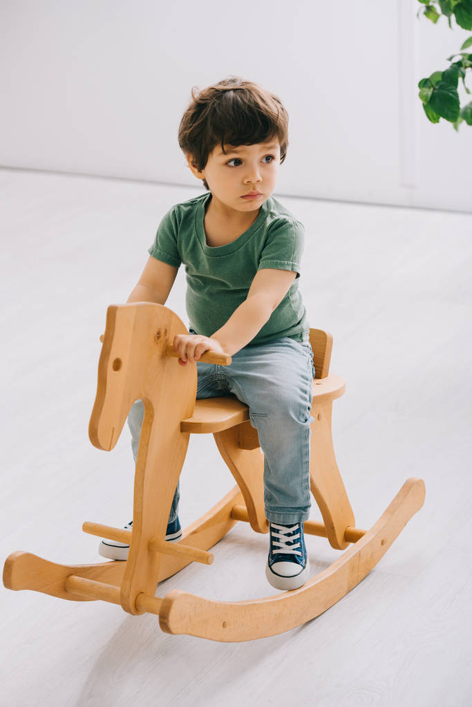 lapsi istuu puinen keinuhevonen olohuoneessa
 - Valokuva, kuva
