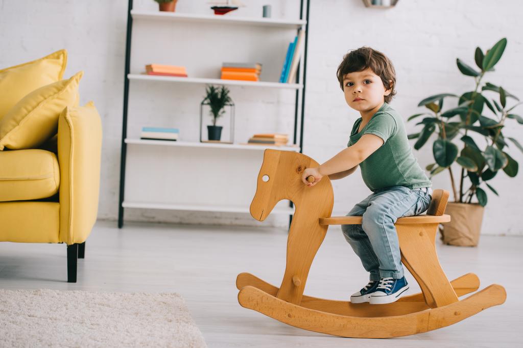 oturma odasında ahşap sallanan at üzerinde oturan çocuk - Fotoğraf, Görsel