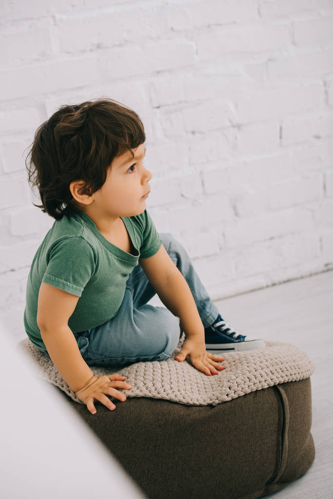 Child in green t-shirt sitting on pouf on floor - Photo, Image