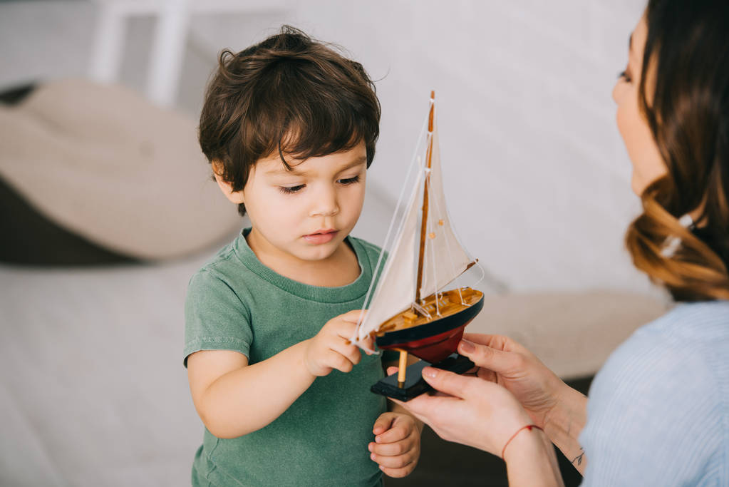 Vista recortada de la madre y el pequeño hijo con barco de juguete
 - Foto, Imagen
