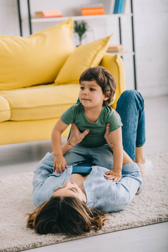 Boldog anya és fia játszik a szőnyegen a nappaliban - Fotó, kép