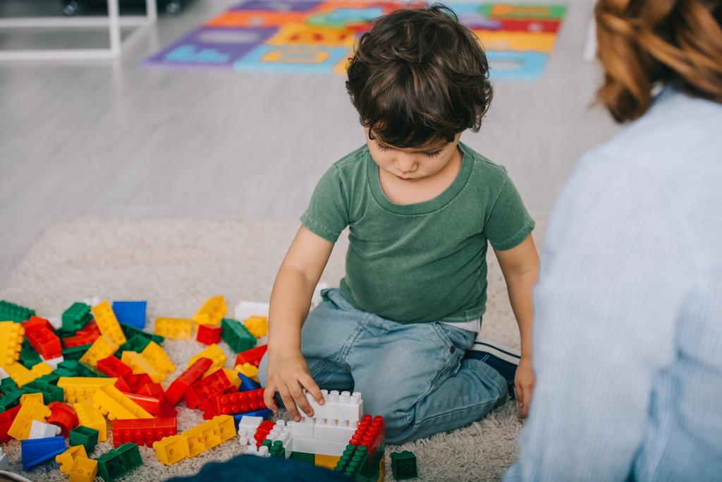 bijgesneden beeld van moeder en zoon spelen met Lego op tapijt in de woonkamer - Foto, afbeelding