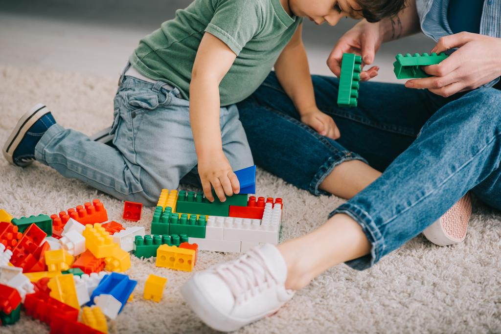 abgeschnittene Ansicht von Mutter und Sohn beim Spielen mit Lego auf Teppich im Wohnzimmer - Foto, Bild