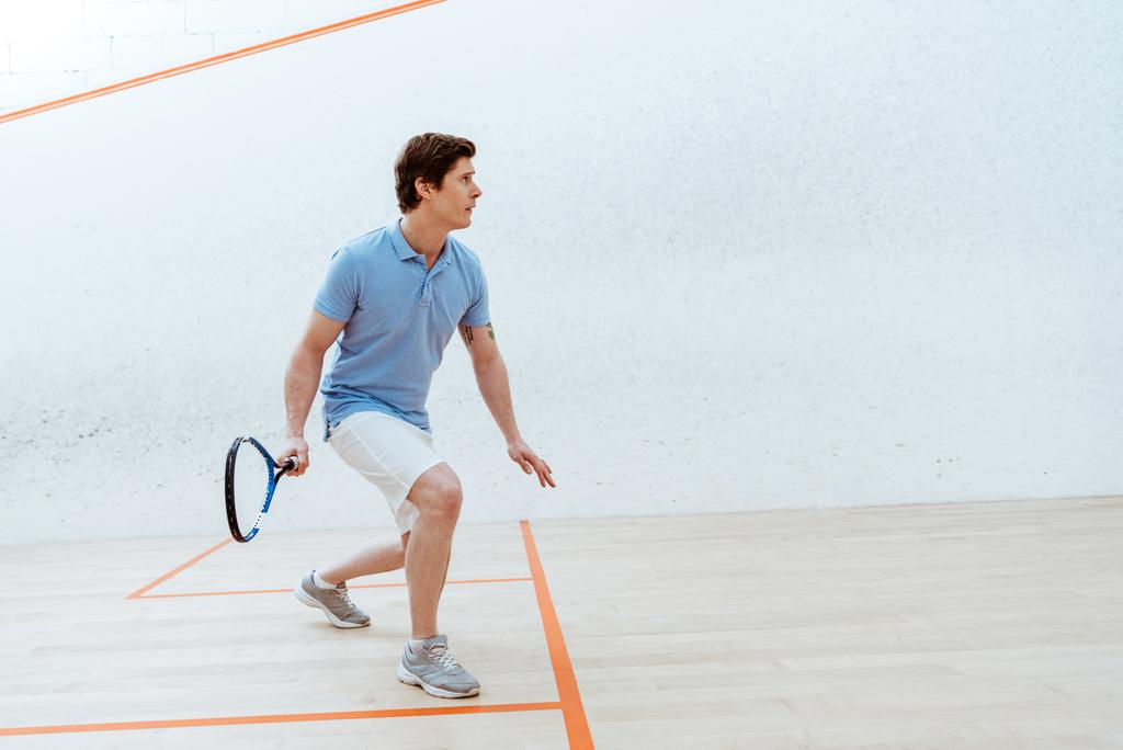 Skoncentrowany sportowiec w niebieskiej koszulce Polo grając w squasha w centrum sportowym - Zdjęcie, obraz