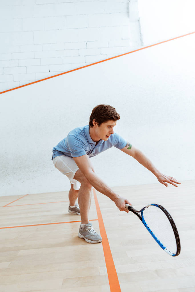 Sportivo emotivo in polo blu che gioca a squash in campo a quattro pareti
 - Foto, immagini