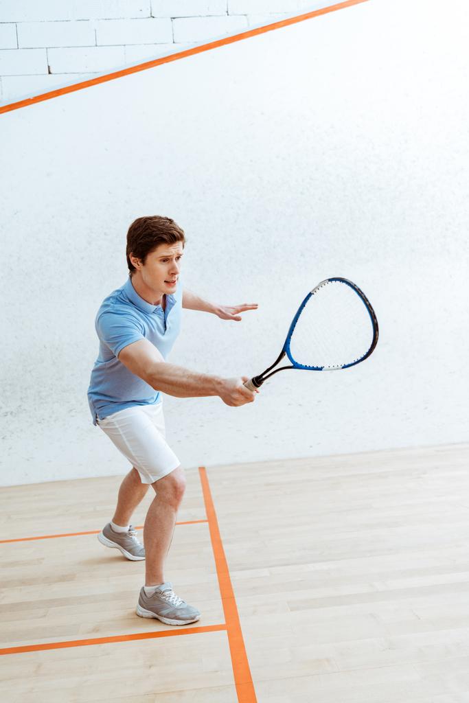Desportista emocional em camisa de pólo azul jogando squash em quadra de quatro paredes
 - Foto, Imagem
