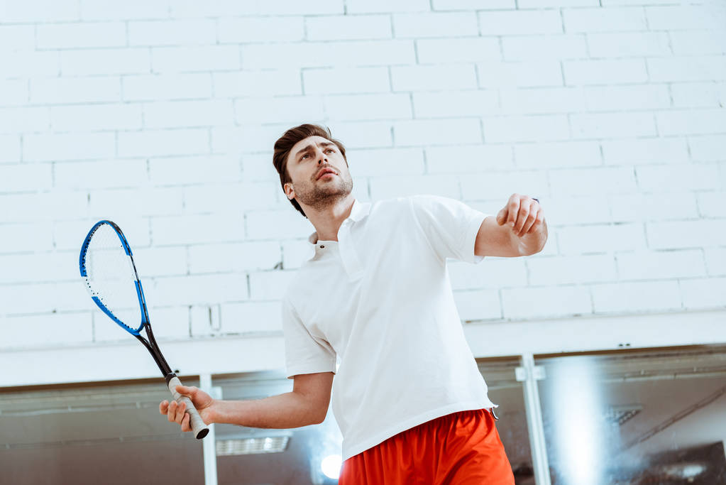 Dört duvarlı kortta squash oynayan beyaz polo gömlekli sporcu - Fotoğraf, Görsel
