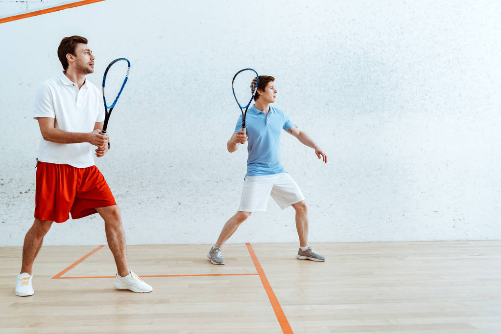 Ganzkörperansicht von zwei Sportlern, die Squash auf einem vierwandigen Platz spielen - Foto, Bild