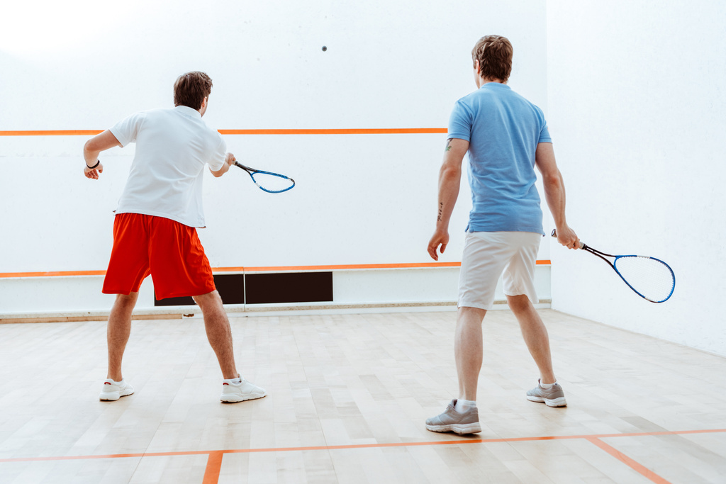 Achteraanzicht van twee sporters die squash spelen in een vierwandige rechtbank - Foto, afbeelding