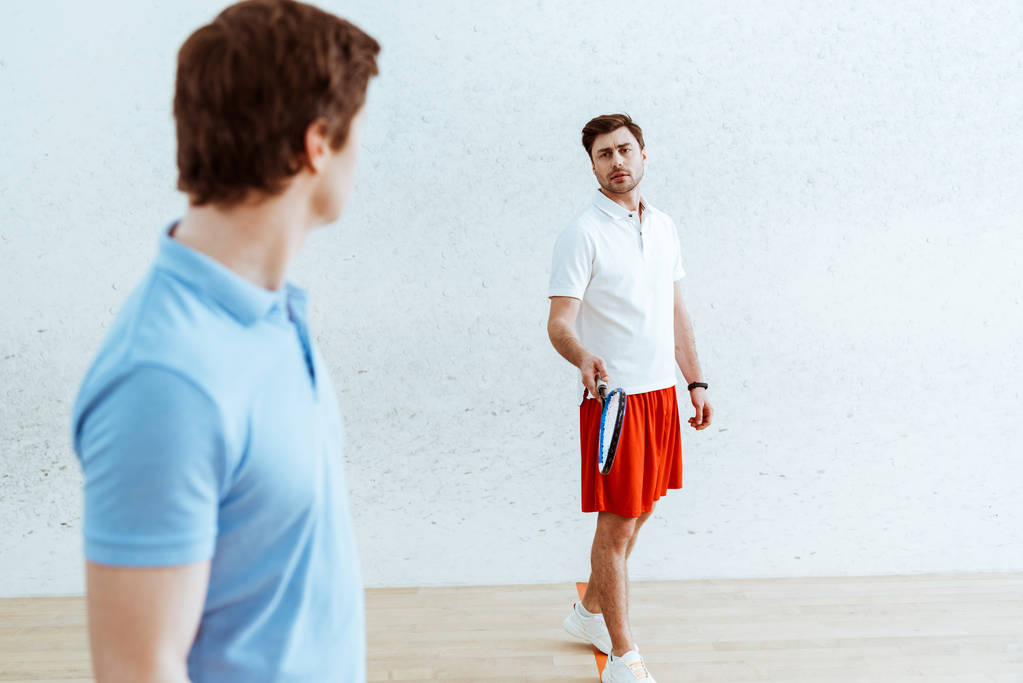 Jogadores de squash em camisa de pólo olhando um para o outro em quadra de quatro paredes
 - Foto, Imagem