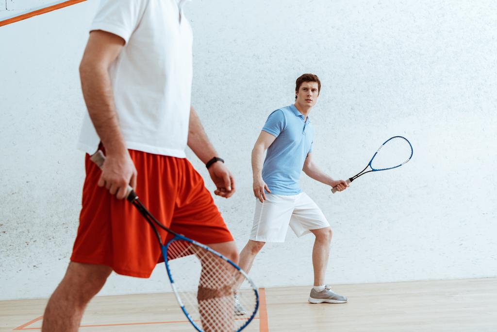 Vista recortada de jugadores de squash con raquetas en cancha de cuatro paredes
 - Foto, imagen
