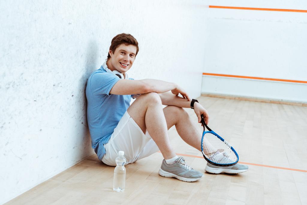 Riendo jugador de squash sentado en el suelo y mirando a la cámara
 - Foto, Imagen